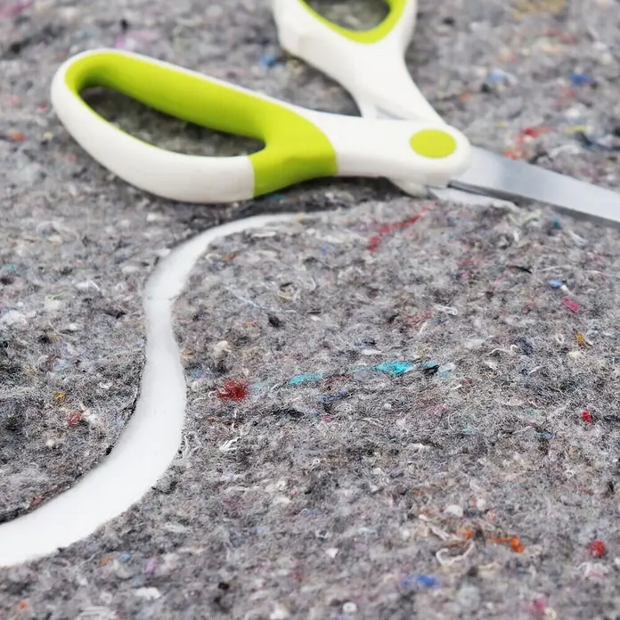 Aquagart Bodenschutzvlies 24m² 500g/m² Teichvlies Teich Schutzvlies -  - Grün-weiß gefärbte Schere schneidet durch grauen, gesprenkelten Stoff und hinterlässt eine weiße Schnittlinie.