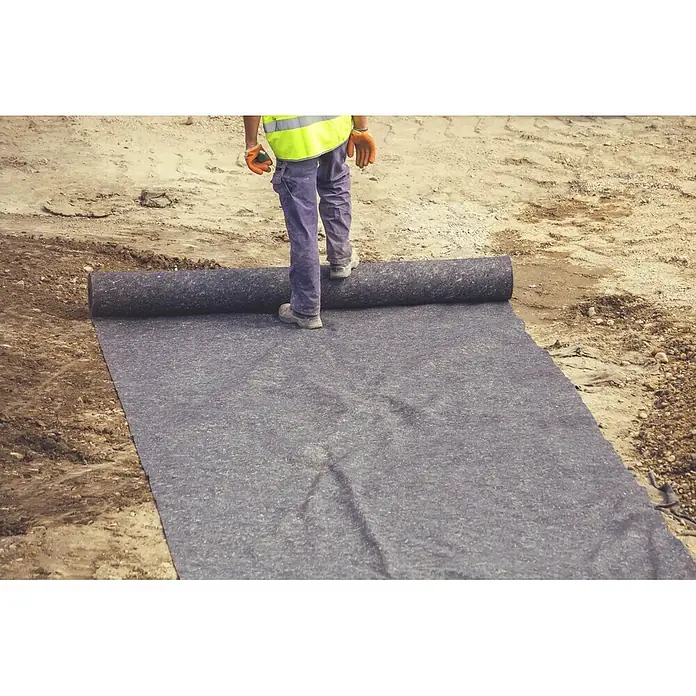 Aquagart Bodenschutzvlies 24m² 500g/m² Teichvlies Teich Schutzvlies -  - Arbeiter rollt dunkles Geotextilvlies auf sandigem Baugrund aus.