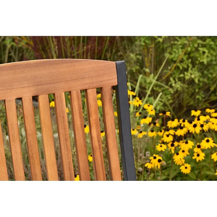Merxx Gartenstuhl Athos - Aluminium/Akazie, Klappbar, graphit/natur - Rückenlehne eines Holz-Gartenstuhls mit schwarzem Metallrahmen, umgeben von gelben Blumen.