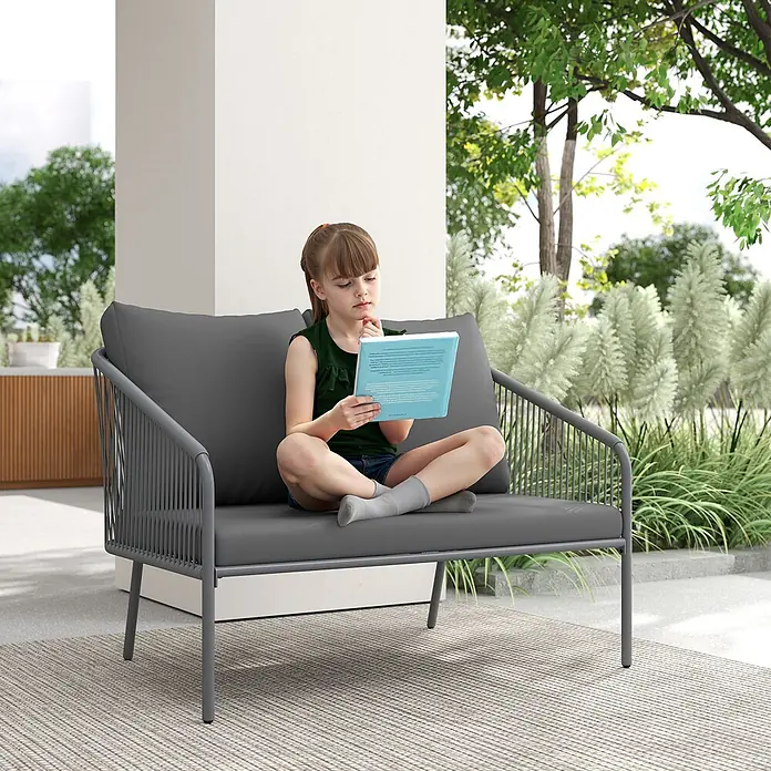 Outsunny Gartenbank - B x T x H: 72 x 72 x 76 cm, Stahl, PE-Rattan, Polyester, Schaumstoff, Grau - Graues Outdoor-Sofa mit geflochtenen Armlehnen und Kissen, ein Mädchen liest ein Buch darauf.
