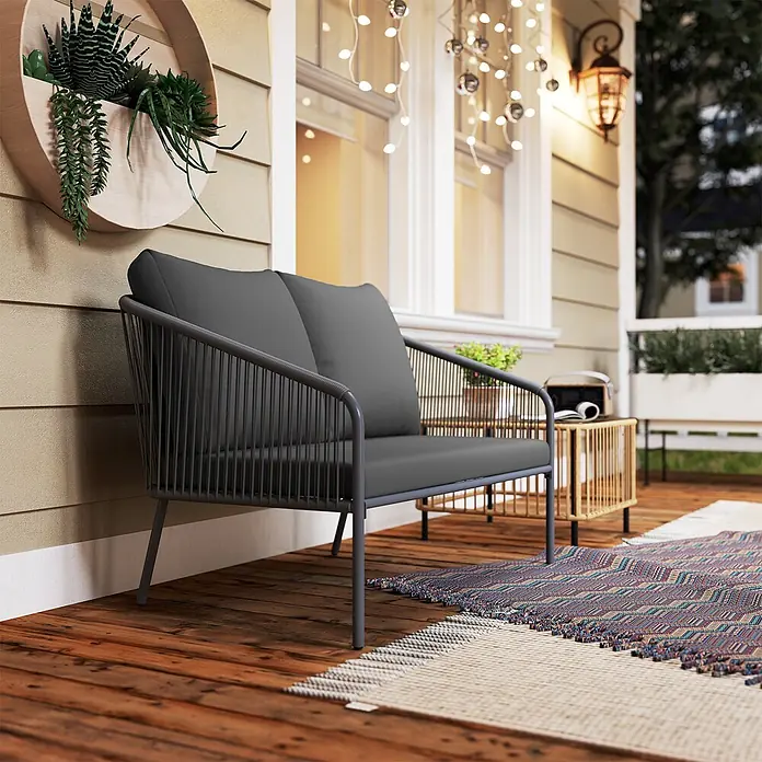 Outsunny Gartenbank - B x T x H: 72 x 72 x 76 cm, Stahl, PE-Rattan, Polyester, Schaumstoff, Grau - Dunkelgraues Outdoor-Zweisitzersofa mit geflochtenen Armlehnen und Rückenlehne auf einer Holzveranda mit buntem Teppich.