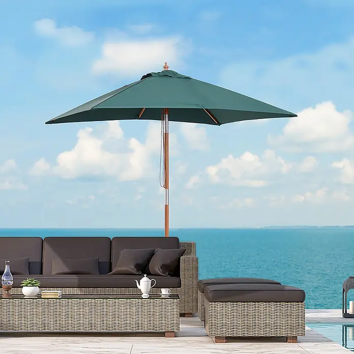 Furnicato Balkonschirm - Grün - Geflochtene Korbmöbel-Garnitur mit dunklen Kissen und grünem Sonnenschirm am Pool mit Meerblick.