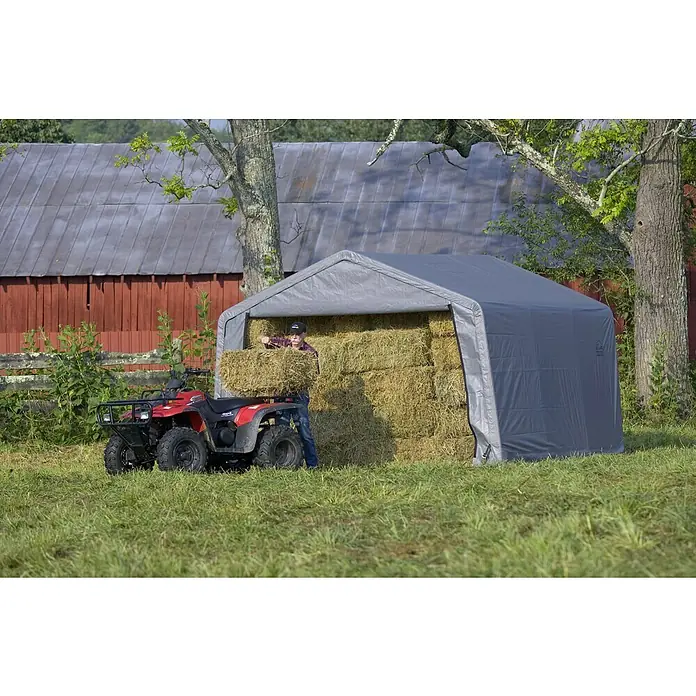 ShelterLogic Gerätehaus - Außenmaß inkl. Dachüberstand (B x T): 370 x 370 cm, Kunststoff, Grau - Ein graues Gerätehaus auf einem Feld, gefüllt mit Heuballen, daneben ein rotes Quad und eine Person, die Heu stapelt.