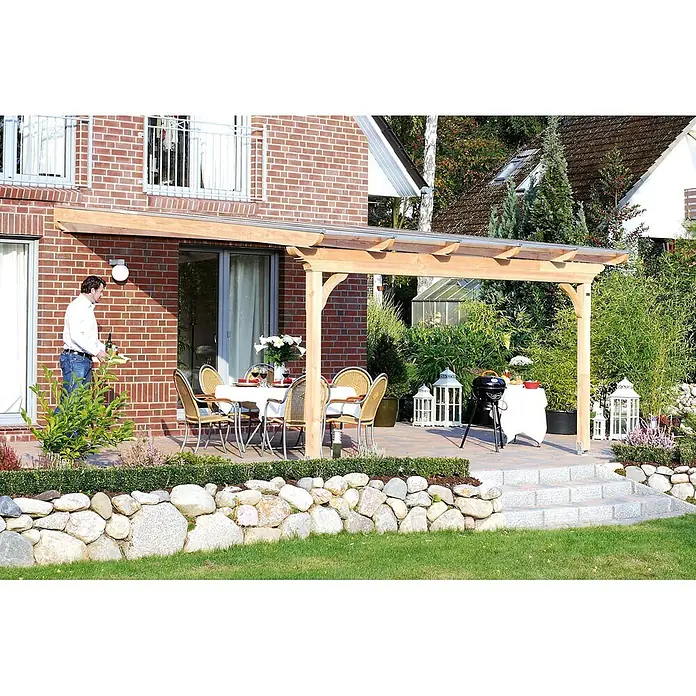 SKAN HOLZ Terrassenüberdachung Ravenna - B x T: 434 x 300 cm, Nussbaum, Polycarbonat, Transparent - Eine helle Holzpergola mit transparentem Dach erstreckt sich von einem Backsteinhaus über eine Terrasse mit Gartenmöbeln.