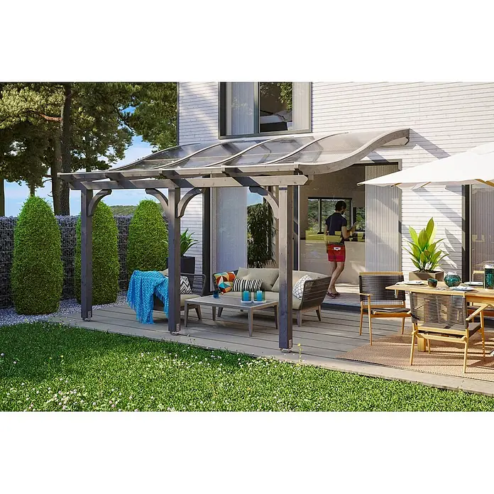 SKAN HOLZ Terrassenüberdachung Venezia - B x T: 434 x 339 cm, Schiefergrau, Polycarbonat, Transparent - Dunkelgraue Pergola mit gebogenem transparentem Dach beschattet einen Outdoor-Loungebereich auf einer Terrasse.