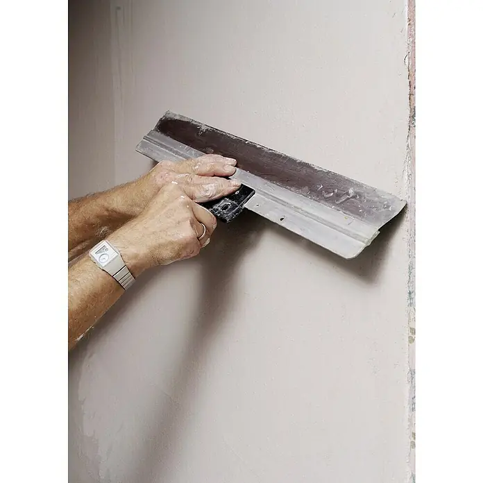 Knauf Rotband Haftputzgips - 30 kg - Nahaufnahme einer Person, die eine Wand mit einem Spachtel glättet, wobei der Fokus auf dem Werkzeug und der Technik liegt.