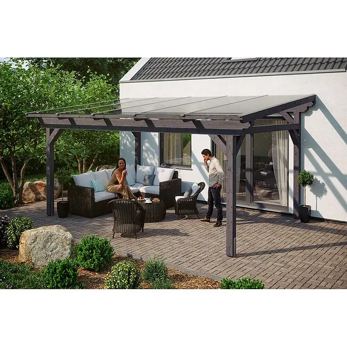 SKAN HOLZ Terrassenüberdachung Sanremo - B x T: 541 x 400 cm, Schiefergrau, Polycarbonat, Transparent - Dunkle Holzpergola mit transparentem Dach über einer Terrasse am Haus, darunter entspannen Menschen.
