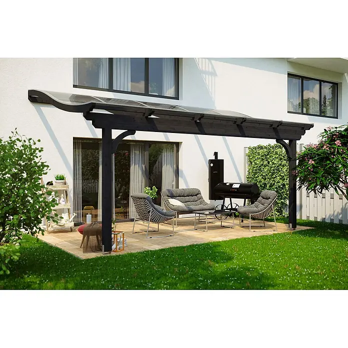 SKAN HOLZ Terrassenüberdachung Verona - B x T: 541 x 239 cm, Anthrazit, Polycarbonat, Transparent - Dunkle Pergola mit durchsichtigem Dach überspannt einen Sitzbereich auf einer Terrasse neben einem weißen Haus.