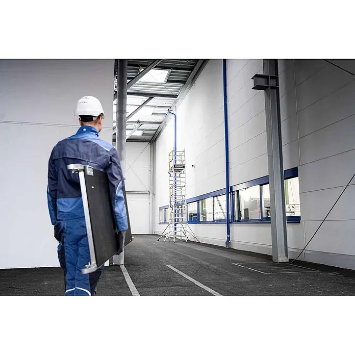 MUNK Rollgerüst FlexxTower SG ergo mit klappbaren Dreieckauslegern und Schwenkfuß Plattformgröße 1,20x0,60m Arbeitshöhe 6,10m -  - Arbeiter trägt eine tragbare schwarz-silberne Arbeitsplattform in Industriehalle.