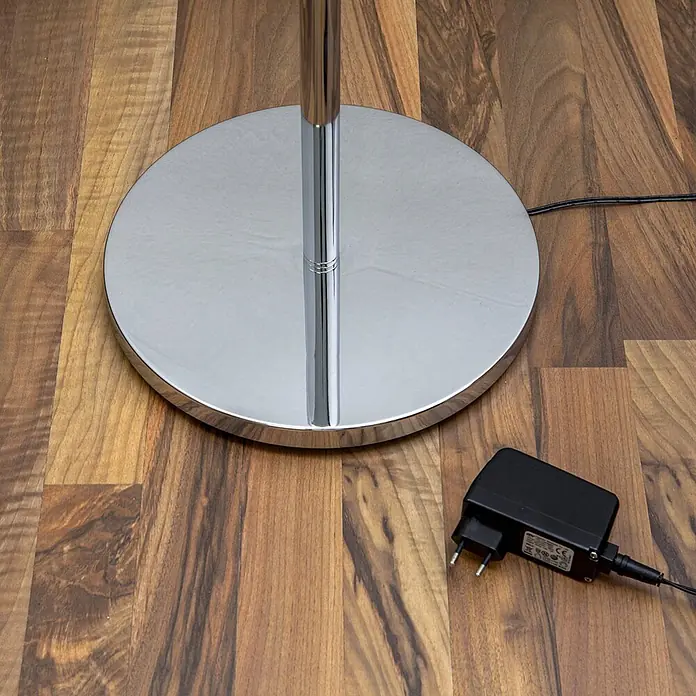 Lindby LED-Deckenfluter Malea - Höhe: 180 cm, chrom / silber, chrom / silber, Warmweiß - Glänzender Chrom-Stehleuchtenfuß mit zentraler Stange und schwarzem Netzteil auf Holzboden.