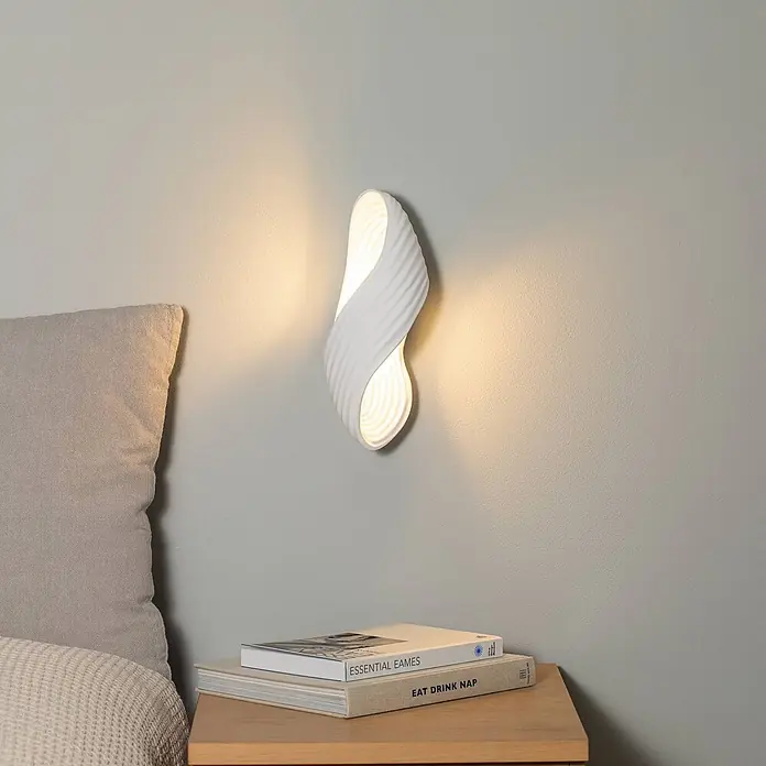 Lindby Wandleuchte Ornela AI - weiß / opal, G9 - Weiße, gewellte Wandleuchte spendet warmes Licht über einem Nachttisch.