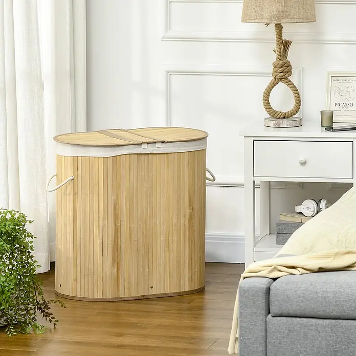 Homcom Allzweck-Korb 100l - Holz, Beige - Ein ovaler Wäschesammler aus Bambus mit Stoffdeckel und Griffen, in einem Wohnraum neben Nachttisch und Sofa.