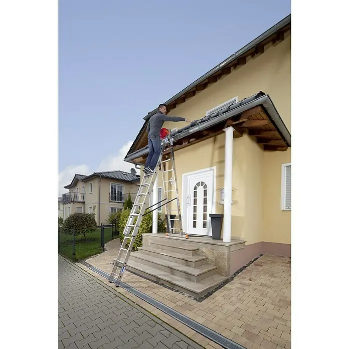 Krause Monto Mehrzweckleiter Tribilo - Arbeitshöhe: 7,65 m, Anzahl Tritte: 30 Stk., Belastbarkeit: 150 kg, Aluminium - Mann auf einer Aluminium-Mehrzweckleiter, der an einem gelben Haus arbeitet. Die Leiter steht auf einer Steintreppe.