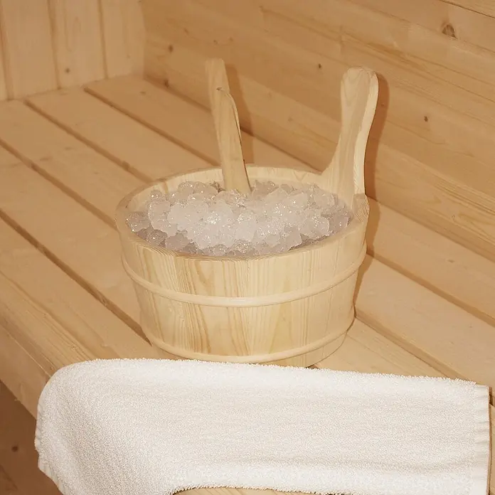 Home Deluxe Fasssauna CUBE DELUXE L - Elektroofen, Holz, L x B x H: 220 x 192,8 x 194 cm - Hölzerner Saunaeimer mit Crushed Ice und Schaufeln, auf einer Holzbank neben einem weißen Handtuch.
