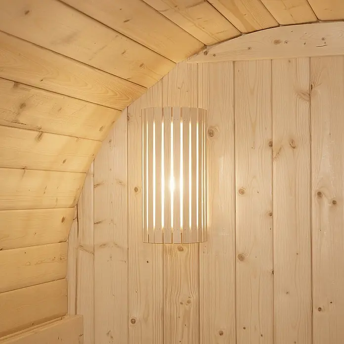 Home Deluxe Fasssauna CUBE DELUXE L - Elektroofen, Holz, L x B x H: 220 x 192,8 x 194 cm - Hölzerne Lampe mit Lamellen an einer hellen Holzwand in einer Sauna.