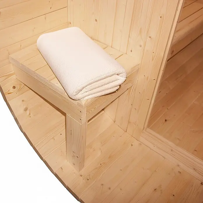 Home Deluxe Fasssauna CUBE DELUXE L - Elektroofen, Holz, L x B x H: 220 x 192,8 x 194 cm - Helle Holzsaunabank mit einem gefalteten weißen Handtuch in einer Holzsauna.
