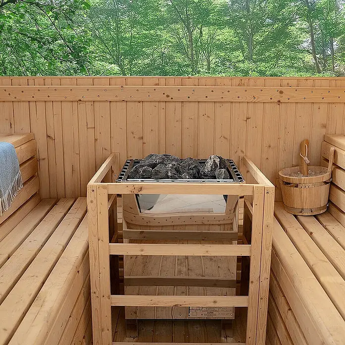 Home Deluxe Fasssauna HYGGE DELUXE Größe: 230 x 220 cm - Elektroofen, Holz, L x B x H: 260 x 230 x 220 cm - Hölzerner Sauna-Innenraum mit Bänken, einem zentralen Elektroofen mit dunklen Steinen und einem Holzeimer mit Schöpfkelle an der Seite.