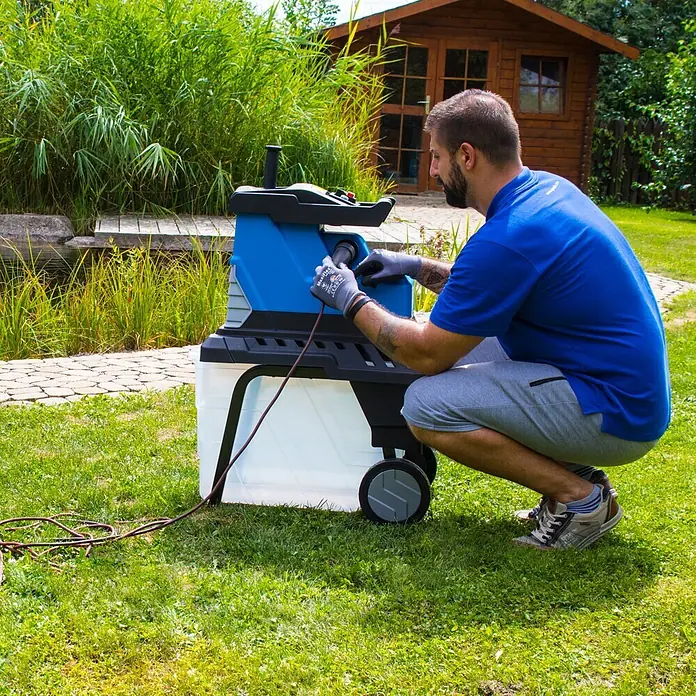 Güde Elektro-Walzenhäcksler GH 2800 Super Silent - Max. Aststärke: 4,5 cm - Mann verbindet Stromkabel mit blau-schwarzem Gartenhäcksler mit transparentem Auffangbehälter.