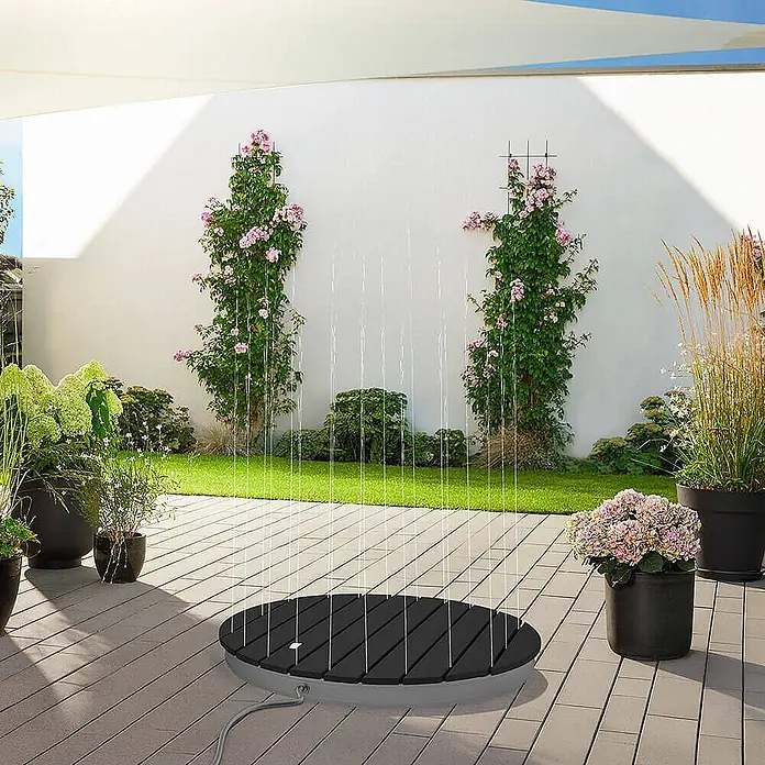 Home Deluxe Bodendusche CALIA - Ø x H: 70,5 x 8 cm, Verbundwerkstoff - Runde, dunkelgraue Latten-Außenduschenbasis mit vertikalen Wasserstrahlen auf einer Terrasse.
