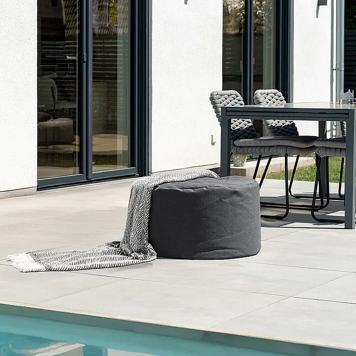 Home Deluxe Gartenhocker CLOUD Pouf - Anthrazit - Dunkelgrauer Outdoor-Pouf mit gemusterter Decke auf heller Terrasse, neben Pool und Essgruppe.