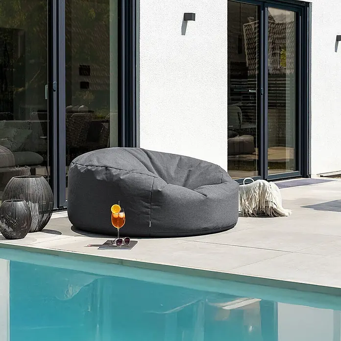 Home Deluxe Gartenhocker CLOUD Pouf - Anthrazit, B x T x H: 140 x 140 x 40 cm - Ein dunkelgrauer Outdoor-Sitzsack aus Stoff auf einer Terrasse am Pool, bereit zum Entspannen.