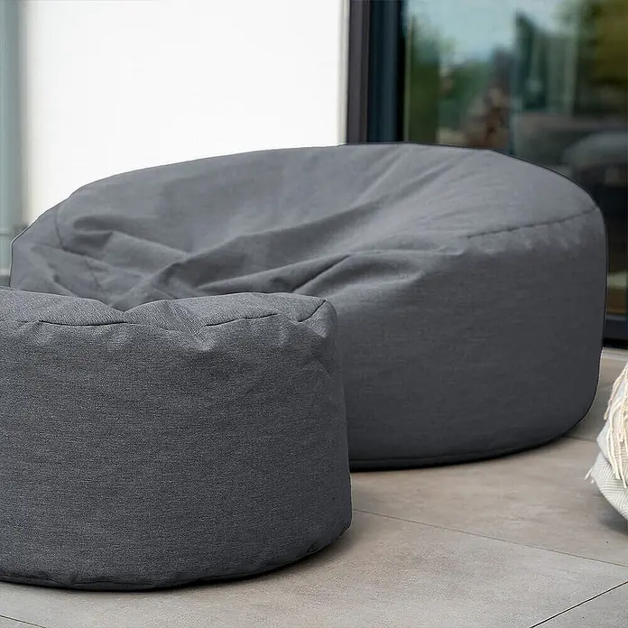 Home Deluxe Gartenhocker CLOUD Pouf Hocker-Set - Anthrazit, B x T x H: 140 x 140 x 40 cm - Zwei graue Stoff-Sitzsäcke, ein großer und ein kleiner, auf einem gepflasterten Außenbereich.