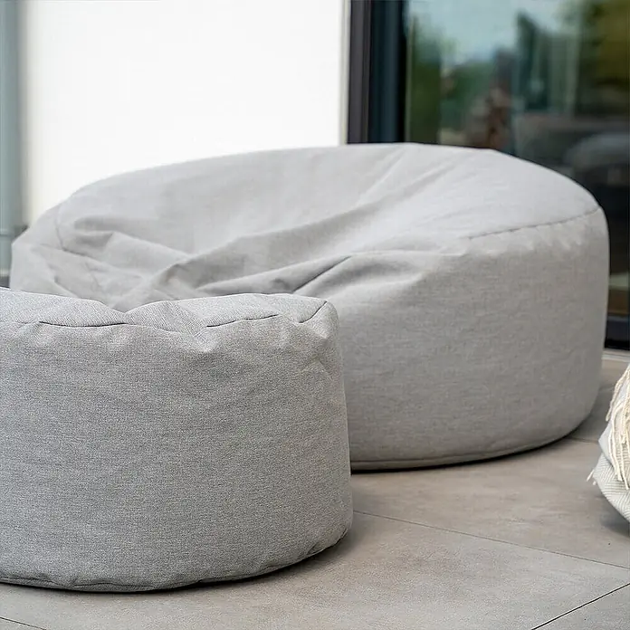 Home Deluxe Gartenhocker CLOUD Pouf Hocker-Set - Hellgrau, B x T x H: 140 x 140 x 40 cm - Zwei hellgraue Stoff-Sitzsäcke, ein großer und ein kleiner, stehen bequem auf einer gefliesten Terrasse.