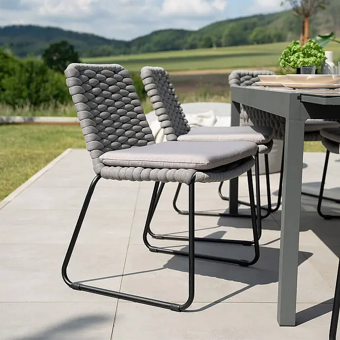 Home Deluxe Gartenstuhl BALERO - 9er Set - Pulverbeschichtet, Hellgrau, B x T x H: 63 x 62 x 85 cm - Graue Outdoor-Esszimmerstühle aus Geflecht mit schwarzen Gestellen und hellgrauen Kissen auf einer Terrasse.