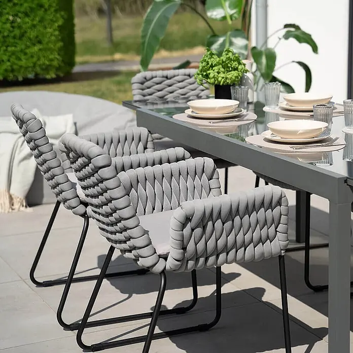 Home Deluxe Gartenstuhl mit Armlehnen BALERO - 7er Set - Pulverbeschichtet, Hellgrau, B x T x H: 63 x 62 x 85 cm - Graue Outdoor-Essstühle aus geflochtenem Seil und passender Tisch, auf der Terrasse für eine Mahlzeit gedeckt.