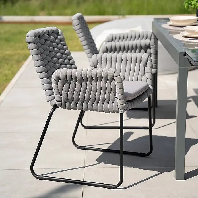 Home Deluxe Gartenstuhl mit Armlehnen BALERO - 7er Set - Pulverbeschichtet, Hellgrau, B x T x H: 63 x 62 x 85 cm - Graue Outdoor-Esszimmerstühle aus geflochtenem Seil mit schwarzen Gestellen und hellen Polstern auf einer Terrasse.