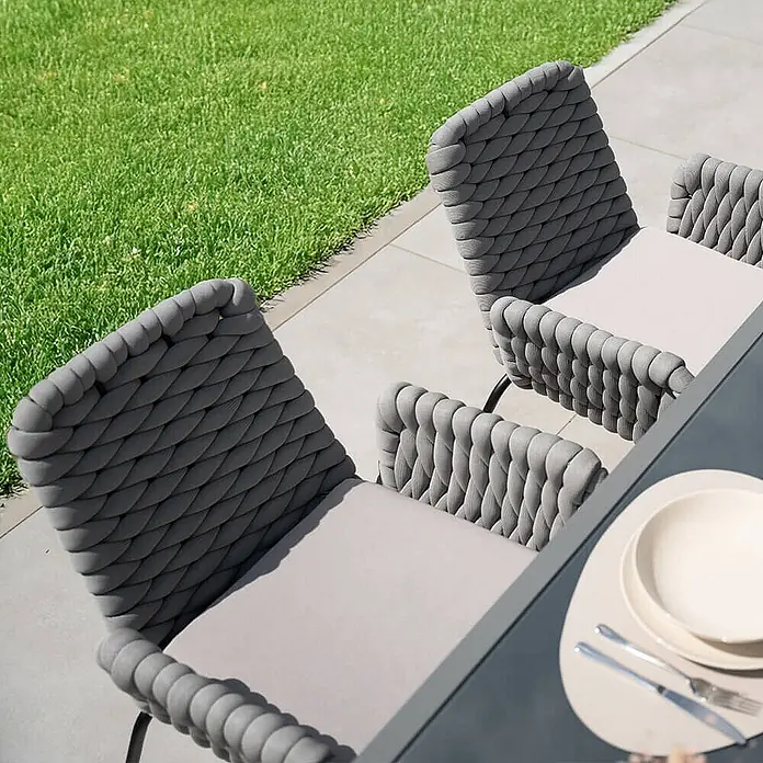 Home Deluxe Gartenstuhl mit Armlehnen BALERO - 7er Set - Pulverbeschichtet, Hellgrau, B x T x H: 63 x 62 x 85 cm - Zwei moderne graue Outdoor-Essstühle mit geflochtenen Rückenlehnen und hellgrauen Kissen an einem Tisch.