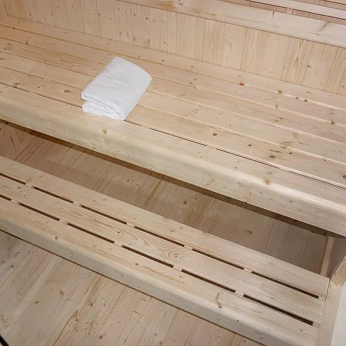 Home Deluxe Elementsauna SHADOW XL - Elektroofen, Steuerung Ofen: Integriert - Helle Holzsaunabänke mit einem gefalteten weißen Handtuch auf der oberen Bank.