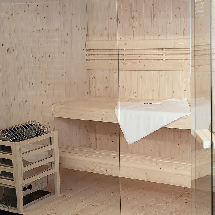 Home Deluxe Elementsauna SHADOW L - Elektroofen, Steuerung Ofen: Integriert, L x B x H: 120 x 150 x 190 cm - Helle Holzsauna innen mit zwei Bänken, einer Rückenlehne und einem Ofen mit Steinen. Ein weißes Handtuch liegt auf der oberen Bank.