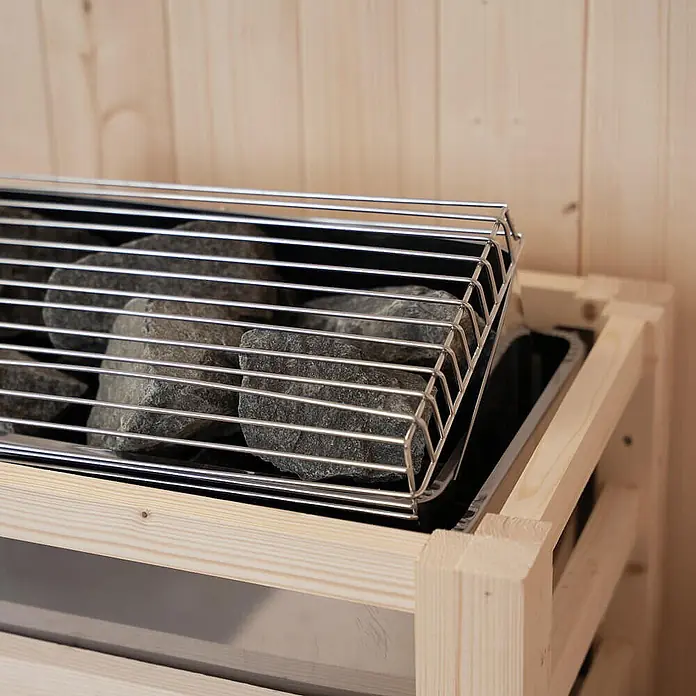 Home Deluxe Elementsauna SHADOW M - Elektroofen, Steuerung Ofen: Integriert, L x B x H: 120 x 120 x 190 cm - Saunaofen mit grauen Steinen und silbernem Metallgitter in einem hellen Holzrahmen in einer Sauna.