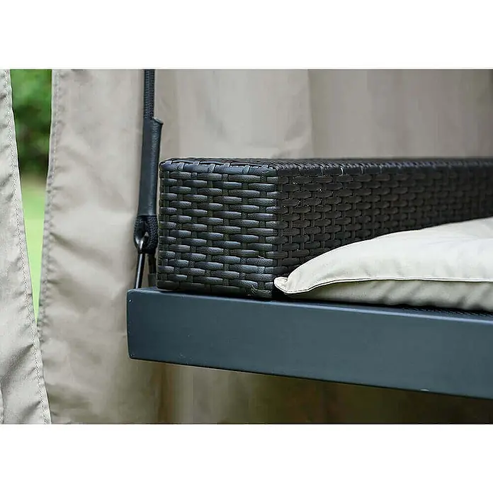 Home Deluxe Gartenliege PROVENCE inkl. Regenabdeckung - Anthrazit, Stahl - Nahaufnahme einer dunkelbraunen geflochtenen Hollywoodschaukel-Armlehne mit hellbeigem Kissen, Teil einer hängenden Gartensitzbank.