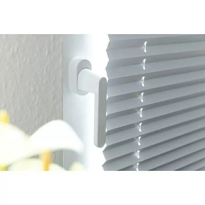 Schellenberg Manilla de ventana con alarma - Blanco, 115 dB - Manija blanca en un marco de ventana junto a estores plisados blancos.