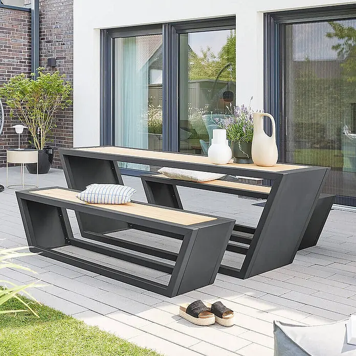 Home Deluxe Gartentisch-Set KOBON - Gesamtumfang: 3 -tlg. - Modernes Outdoor-Esstischset aus dunkelgrauem Metall und Holzoptik mit Tisch und zwei Bänken auf einer Terrasse.