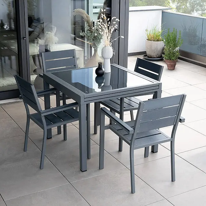 Home Deluxe Gartentisch-Set VERANO MADERA - Gartentisch - Gesamtumfang: 3 -tlg., Ausziehbar - Graues Terrassen-Essgruppe mit Glastisch und vier Stühlen auf einem Balkon.
