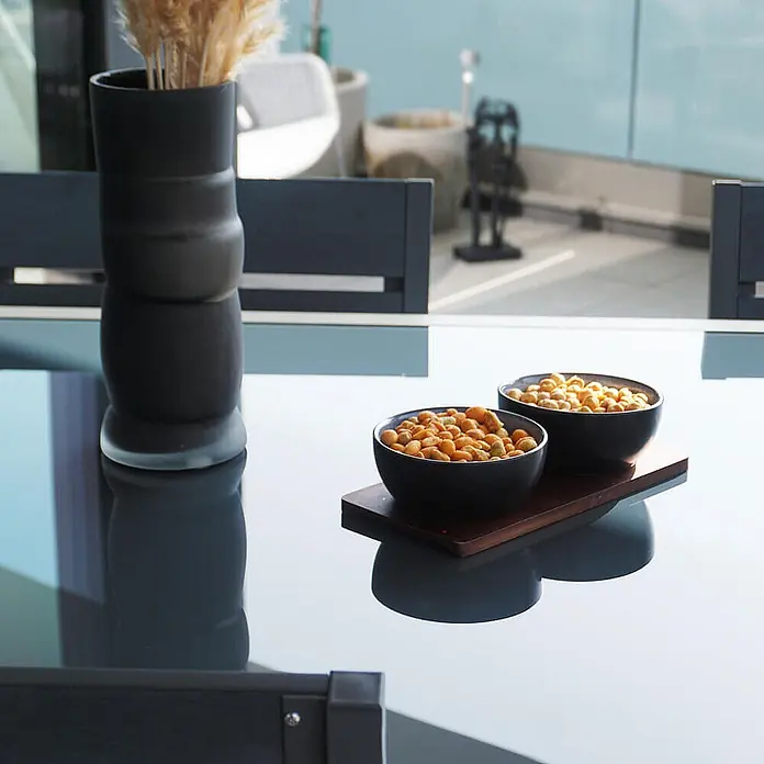Home Deluxe Gartentisch SOL - L x B x H: 70 x 180 x 240 cm, Anthrazit - Zwei schwarze Schalen mit Snacks auf einem Holztablett, auf einem Glastisch serviert.