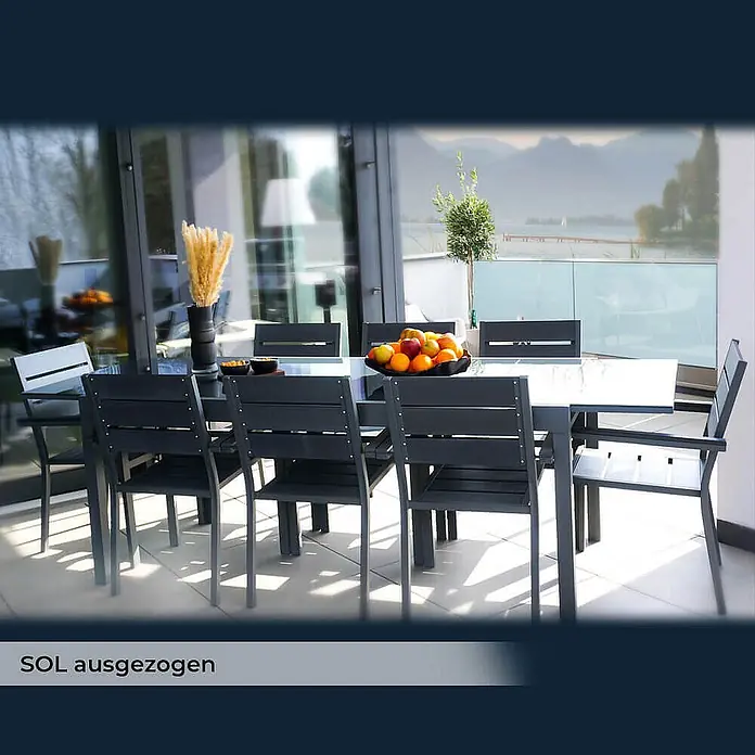 Home Deluxe Gartentisch SOL - L x B x H: 70 x 180 x 240 cm, Anthrazit - Große dunkelgraue Outdoor-Essgruppe mit Stühlen auf einer Terrasse mit See- und Bergblick.