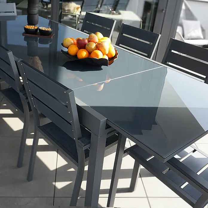 Home Deluxe Gartentisch SOL - L x B x H: 70 x 180 x 240 cm, Anthrazit - Dunkelgrauer Outdoor-Esstisch und passende Stühle, mit dunkler Platte und Metallrahmen, auf einer Terrasse.