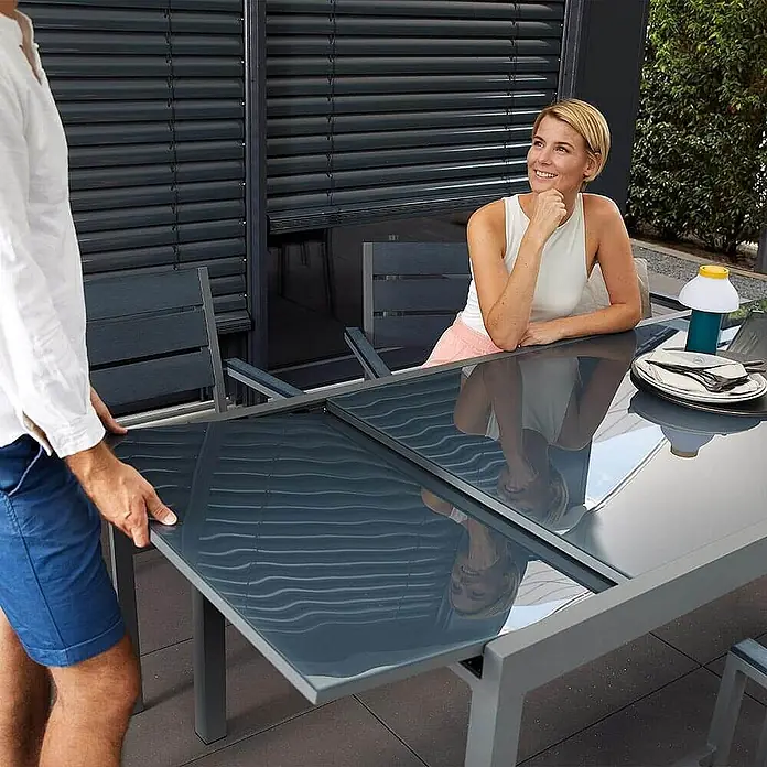 Home Deluxe Gartentisch SOL - L x B x H: 70 x 180 x 240 cm, Anthrazit - Anthrazitgrauer ausziehbarer Gartentisch wird von einer Person verlängert, eine Frau sitzt am anderen Ende.