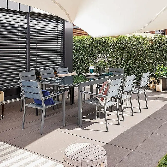 Home Deluxe Gartentisch-Set SOL Menge: 1 tlg. -  - Graues Outdoor-Essset mit Glastisch und Lattenstühlen auf einer Terrasse unter einem Sonnensegel.