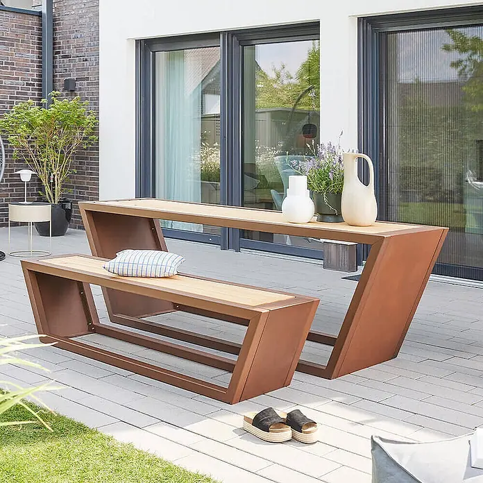 Home Deluxe Gartentisch-Set KOBON - 1x Bank + 1x Tisch - Gesamtumfang: 2 -tlg. - Modernes Outdoor-Essset mit langem Tisch und passender Bank aus Naturholzplatten und markanten rostbraunen Metallgestellen auf einer Terrasse.