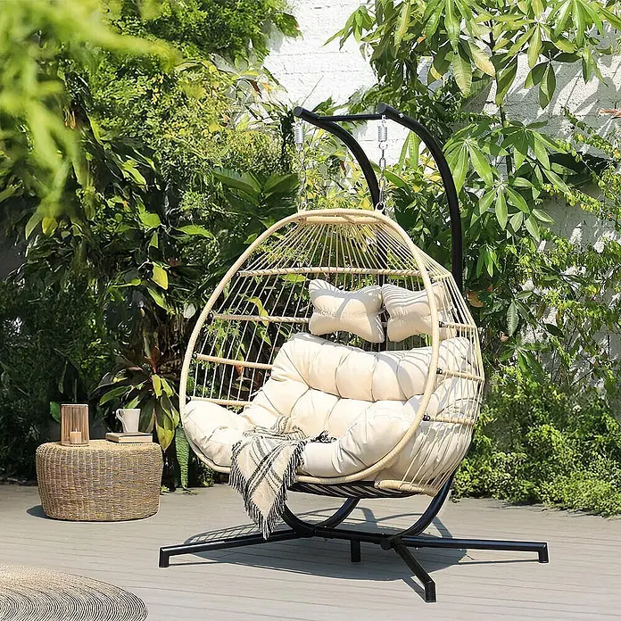 Home Deluxe Hängesessel LOMA 2-Sitzer - Kunststoff, Beige - Beigefarbener Hänge-Eiersessel aus Korbgeflecht mit cremefarbenen Kissen und schwarzem Gestell, auf einer Terrasse.