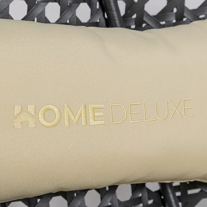 Home Deluxe Hängesessel TWIN DELUXE inkl. Regenabdeckung - L x B x H: 74 x 145 x 126 cm, Schwarz - Helles beiges Kissen mit gesticktem 'HOME DELUXE'-Logo, dessen 'H' ein Haus darstellt, auf dunklen Korbmöbeln.
