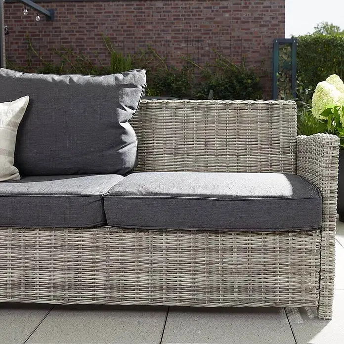 Home Deluxe Polyrattan Sitzgruppe BAHIA Ohne Regenabdeckung -  - Hellgraues Rattan-Gartensofa mit dunkelgrauen Kissen auf einer Terrasse.