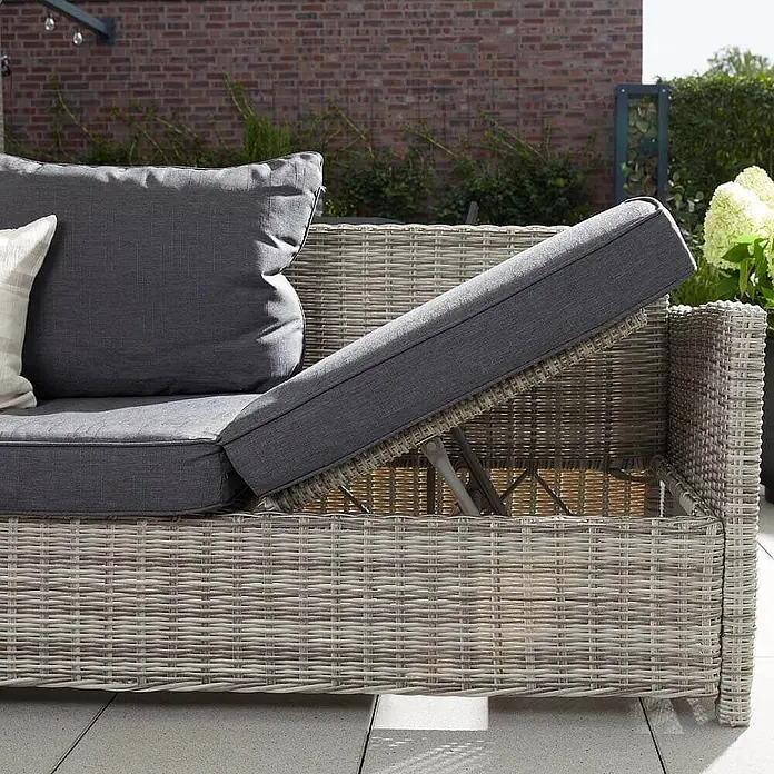Home Deluxe Polyrattan Sitzgruppe BAHIA Ohne Regenabdeckung -  - Helles graues Outdoor-Sofa in Rattan-Optik mit dunklen Kissen, dessen aufklappbarer Teil Stauraum zeigt.
