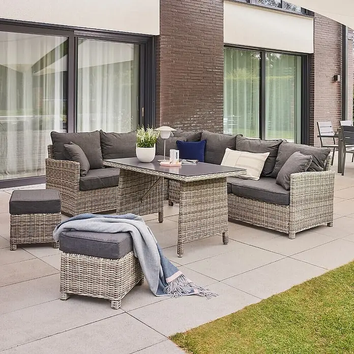 Home Deluxe Polyrattan Sitzgruppe BAHIA Ohne Regenabdeckung -  - Graue Rattan-Lounge-Garnitur für den Außenbereich mit dunklen Kissen auf einer Terrasse, bestehend aus Ecksofa, Tisch und zwei Hockern.