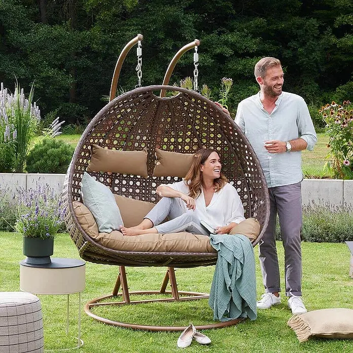 Home Deluxe Hängesessel TWIN - Kunststoff, Braun - Brauner Rattan-Hänge-Eiersessel mit beigen Kissen, zur Entspannung im Garten genutzt.